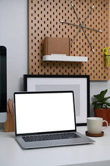 Mock up computer laptop with blank screen and office supplies on white desk at modern home office.