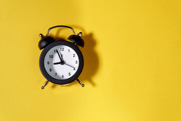 black alarm clock on yellow background. copy space. flat lay