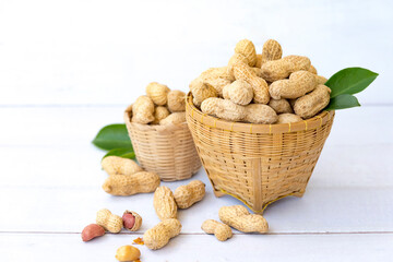 Peanuts with leaf in wooden basket and peanuts in the peel scattered isolated on wooden white background.Healthy vegetarian concept.