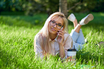 sexy blonde woman talking on the mobile phone and lying on meadow