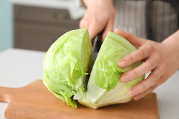 Woman cutting iceberg lettuce on table in kitchen, closeup