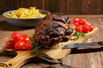 Baked lamb leg on wooden cutting board with garnish