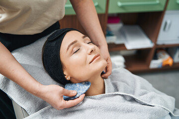Beauty salon customer with eyes shut undergoing a gua sha treatment