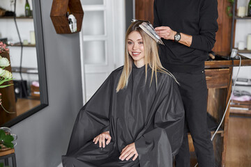 Naklejka premium Confident male stylist is dyeing hair of blond caucasian female client