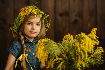 Beautiful girl with a wreath of mimosa flowers on her head. Bouquet of flowers