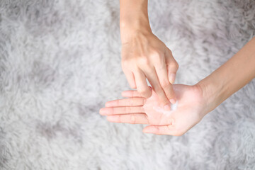 Woman applying moisturizing hand cream on hand with carpet background, Health care concept.