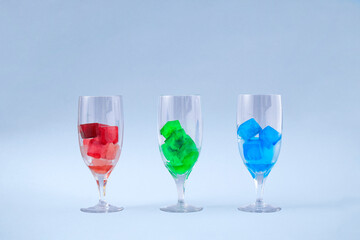 Creative concept of three wine glasses with rgb ice in them. Ice red, green and blue cocktails on grey background..