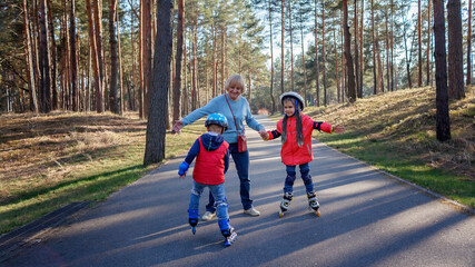 Happy kids riding on roller skates together with grandmother at park, hugs and support, active...