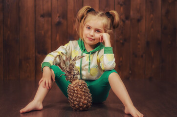 Beautiful and cute baby girl sitting on the floor in her hands a pineapple