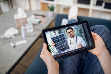 Unrecognizable female patient having video chat with male doctor on digital tablet at home, getting online consultation. Telemedicine and remote medical services.