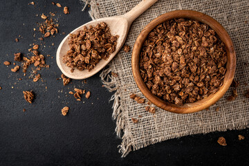 Chocolate granola in wooden bowl on black background.