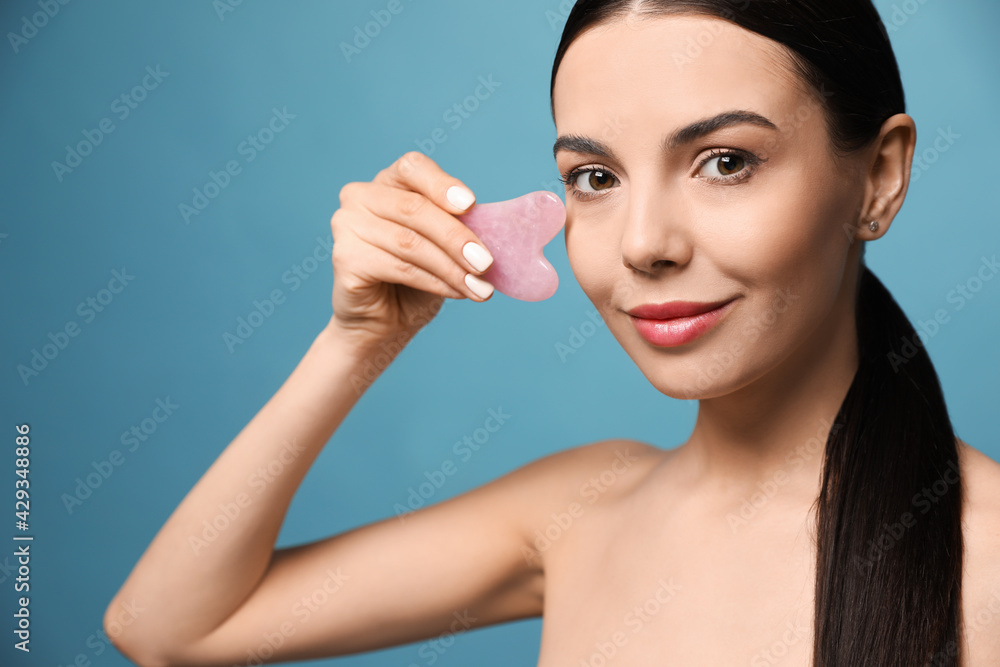 Canvas Prints Beautiful young woman doing facial massage with gua sha tool on blue background, closeup