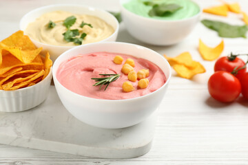 Different kinds of tasty hummus, nachos and ingredients on white wooden table