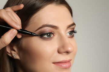 Artist applying black eyeliner onto woman's face on grey background, closeup