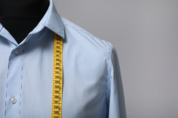 Semi-ready shirt with tailor's measuring tape on mannequin against grey background, closeup. Space for text