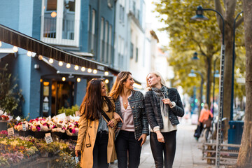 Three young women walking together trough city.