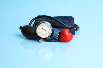 Blood pressure meter and toy heart on light blue background