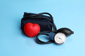 Fototapeta na wymiar Blood pressure meter and toy heart on light blue background
