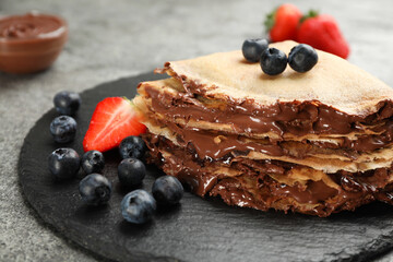 Delicious thin pancakes with chocolate paste and berries on slate plate, closeup