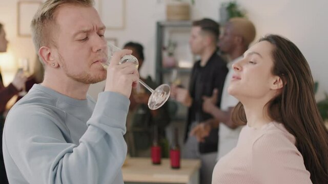 Close up shot of happy young man and woman holding glasses of white wine and dancing together at house party