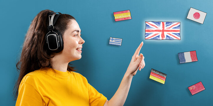 Online language learning. Portrait of a young smiling woman wearing headphones, pointed with her finger on the English flag. Blue background with different flags. Concept of English language day