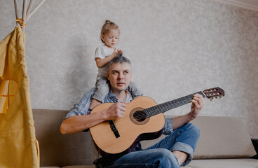cute little girl and her handsome father play guitar and smile sitting on the couch at home. father's day.