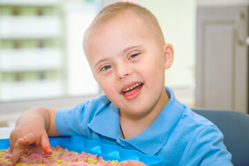 Portrait of a cute boy with Down syndrome, a child playing with sand and molds for modeling, early...