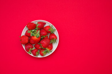 Flat lay of strawberries on a plate against red background