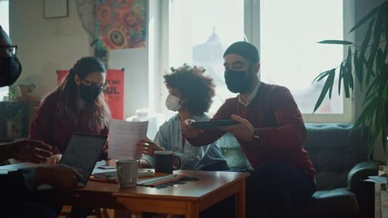 Team of Young Professionals Wearing Face Masks, Talking on a Meeting in Modern Creative Office. Diverse Team of Social Media Marketing Specialists Brainstorm, Share Data on Tablet Computer, Innovate - Powered by Adobe