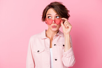 Photo portrait of kissing woman looking at blank space in rose-tinted heart-shaped glasses isolated on pastel pink colored background