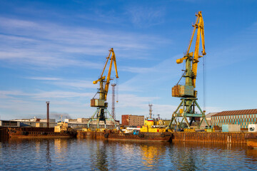 Fototapeta na wymiar Cargo seaport. View of old harbor cranes and rusty ships near the pier. Sea port in the Arctic. Industry and infrastructure in the Far North of Russia. Beringovsky, Chukotka, Siberia, Russia.