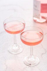 Two glasses of pink rose wine with bottle on white marble background