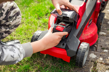 Teenager changes rechargeable battery in electric lawn mower