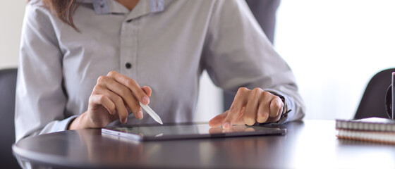 Businessperson hand with stylus pen touching on digital tablet on round black table