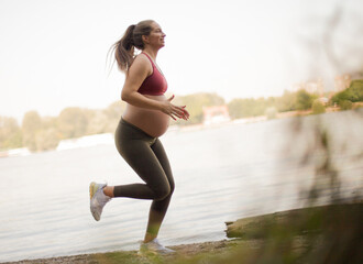 Pregnant woman jogging by the lake. - 429354817