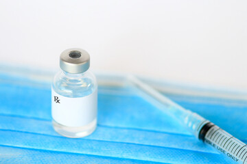 Medical vial of injectable medicine and hypodermic needle on a blue mask