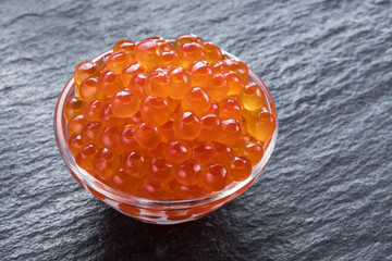 Red caviar in the bowl on gray graphite background.