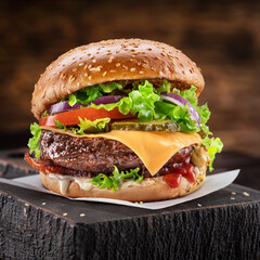 Delicious burger with cola and potato fries on a wooden table with a dark brown background behind. Fast food concept.