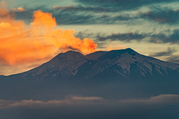 The silhouette of Mount Etna smoking in orange by the sunset light 
