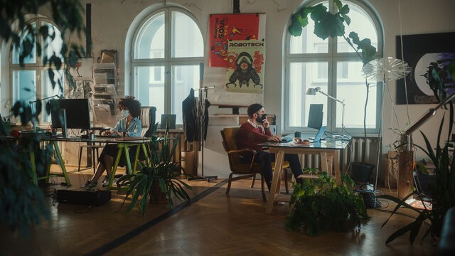 Creative Modern Office with Two Young People Wearing Face Masks Working on Computers. Authentic Content Creators, Game Software Developers, Marketing Specialists Creating Content. Wide Elevated Shot
