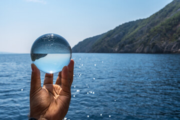 Crystal ball in the man’s hand. Original upside down view and rounded perspective of the sky and sea. © volff