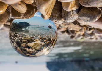 Crystal ball on pebbles near the sea. Original upside down view and rounded perspective of the sky, sea and boat.