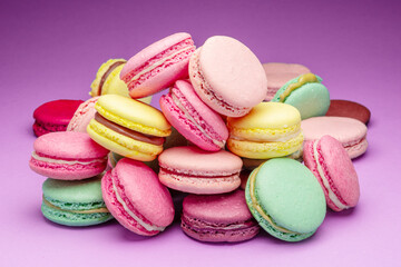 Fototapeta na wymiar Colorful sweet macarons or macaroons, flavored cookies on purple background.