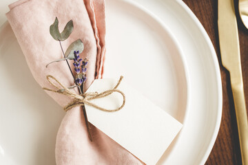 Close up view on plates arranged with a pink linen napkin, floral decor and tag.