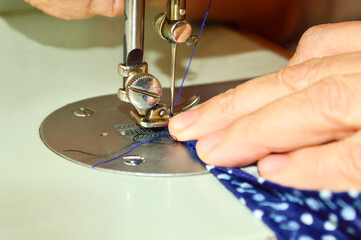 close-up - a woman's hand at work on a sewing machine, sews from blue material