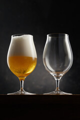 Glass with light golden beer and empty glass on a dark background
