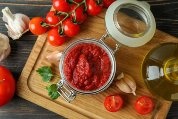 Jar with tomato paste on wooden table with ingredients