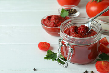 Bowl and jar with tomato paste on white wooden background with ingredients