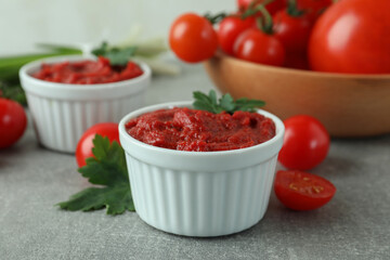 Bowls with tomato paste on gray background with ingredients