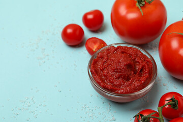 Bowl with tomato paste, tomatoes and salt on blue background